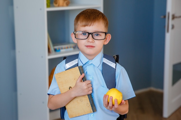 Écolier avec des lunettes tient un livre et une pomme à l'école