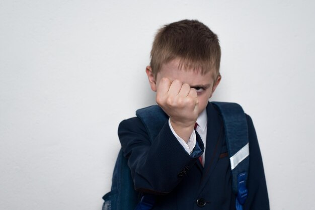 Écolier menace avec son poing Garçon en uniforme scolaire Fond blanc Bagarreur