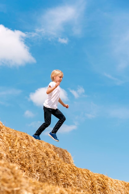 Écolier pendant le saut Enfant court et saute sur la botte de foin Récolte du foin Récolte Vacances d'été