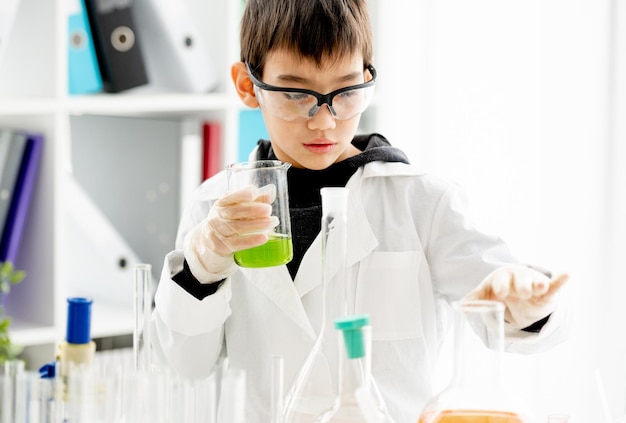 Écolier portant des lunettes de protection faisant une expérience de chimie regardant un tube dans une classe de sciences élémentaires Élève intelligent analysant un liquide en laboratoire pendant le test