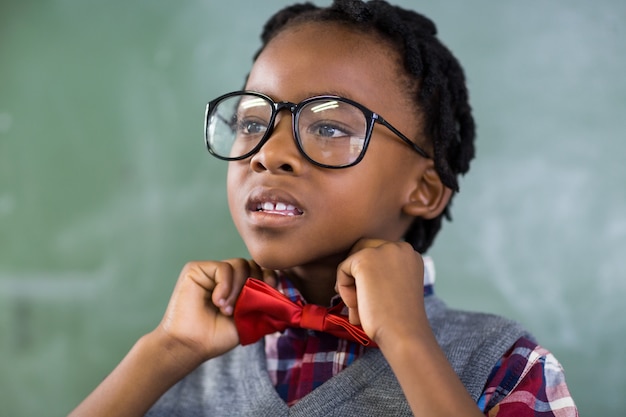 Écolier réfléchi en ajustant un noeud papillon en classe