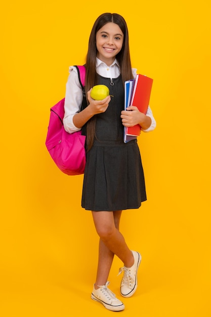 Écolière adolescente étudiante avec sac à dos sac d'école tenir aplle et livres sur fond de studio isolé jaune Concept d'école et d'éducation des enfants