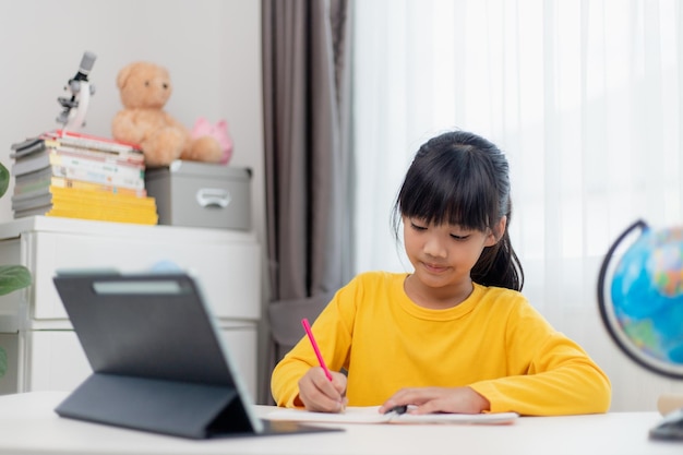 Écolière asiatique faisant ses devoirs avec une tablette numérique à la maison Les enfants utilisent des gadgets pour étudier Éducation et apprentissage à distance pour les enfants Enseignement à domicile pendant la quarantaine Rester à la maison