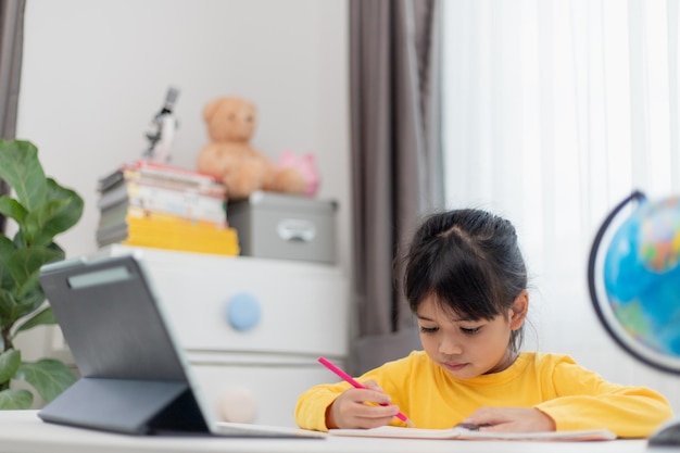 Écolière asiatique faisant ses devoirs avec une tablette numérique à la maison Les enfants utilisent des gadgets pour étudier Éducation et apprentissage à distance pour les enfants Enseignement à domicile pendant la quarantaine Rester à la maison