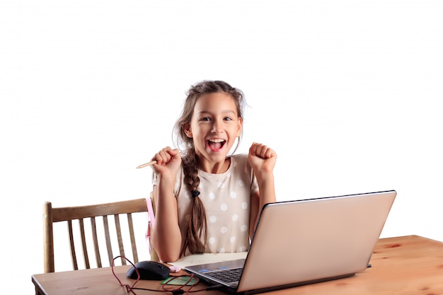 Écolière assis à une table avec un ordinateur portable avec un visage émotionnel expressif