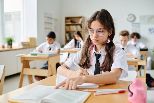 Écolière assise à son bureau et lisant un manuel pendant la leçon à l'école