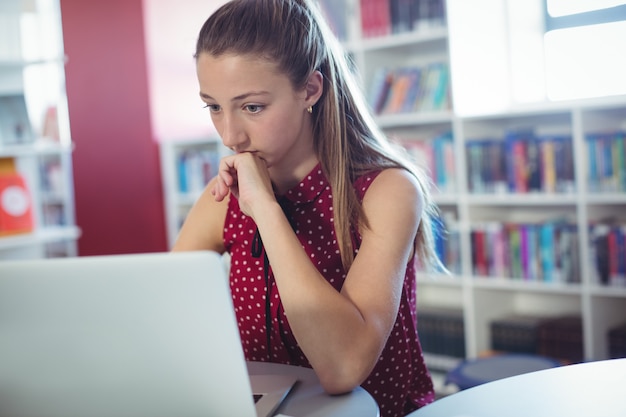 Écolière attentive à l'aide d'un ordinateur portable dans la bibliothèque