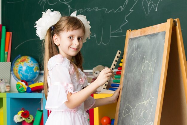 Écolière des classes primaires. Dessinez au tableau noir. L'éducation à l'école. Fille avec des arcs