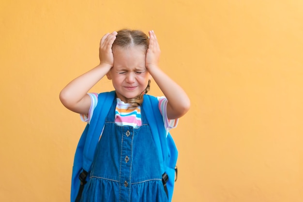 Écolière en colère et fatiguée avec sac d'école en uniforme isolé sur fond jaune. frustré