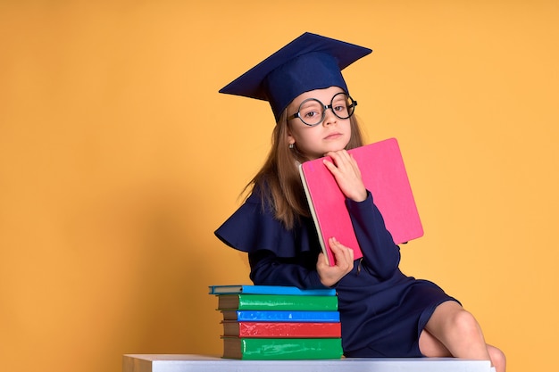 Écolière curieuse en tenue de graduation étudie avec des manuels