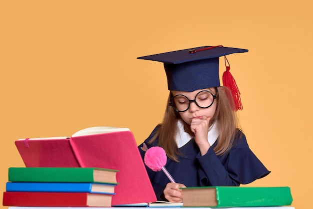 Écolière curieuse en tenue de graduation étudie avec des manuels