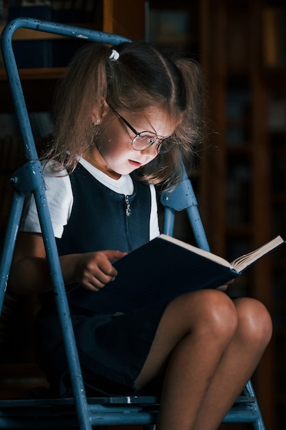 Écolière sur l'échelle dans la bibliothèque pleine de livres