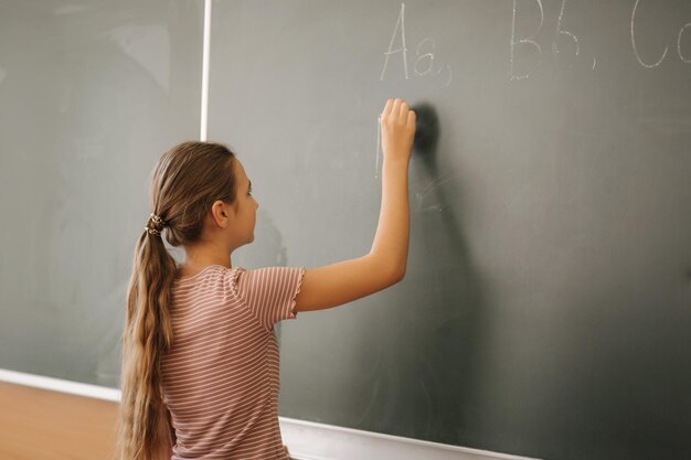 Écolière écrivant quelque chose sur le tableau noir dans la salle de classe