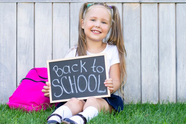 Écolière est assise sur l'herbe, sac à dos scolaire