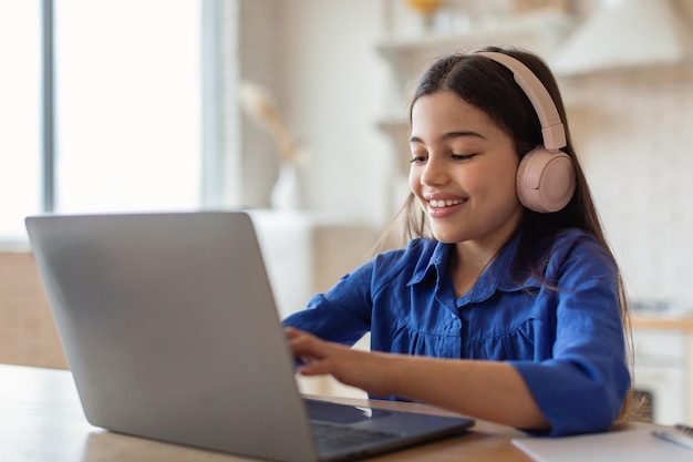 Écolière étudiant la saisie en ligne sur un ordinateur portable portant des écouteurs à la maison