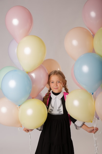 Écolière de fille, élève de première année dans l'uniforme scolaire sur un fond blanc avec des boules et des fleurs