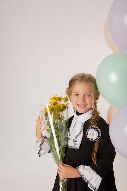 Écolière de fille, élève de première année dans l'uniforme scolaire sur un fond blanc avec des boules et des fleurs