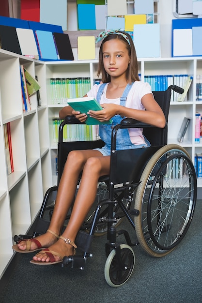Écolière handicapée en fauteuil roulant tenant un livre dans la bibliothèque