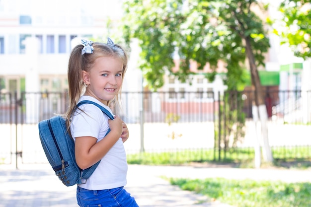 Écolière heureuse avec un sac à dos dans un t-shirt blanc. dans la rue