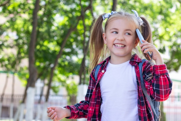 Écolière heureuse avec un sac à dos, parler au téléphone