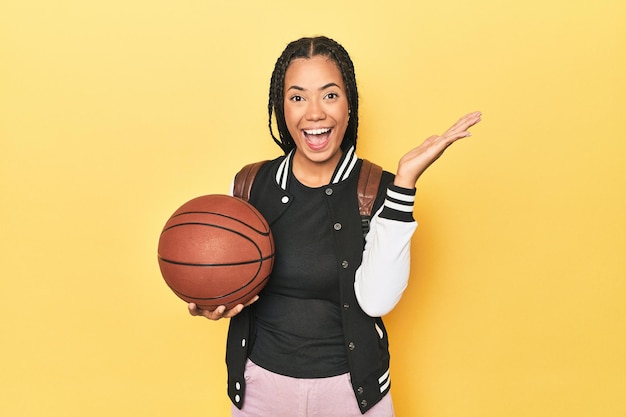 Écolière indonésienne avec basket-ball sur jaune recevant une agréable surprise excitée