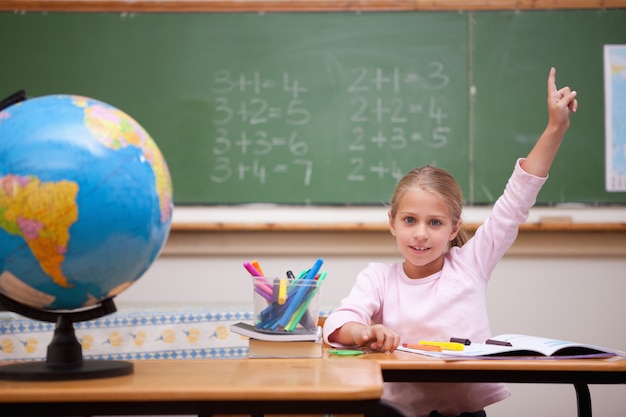 Écolière mignon levant la main pour répondre à une question