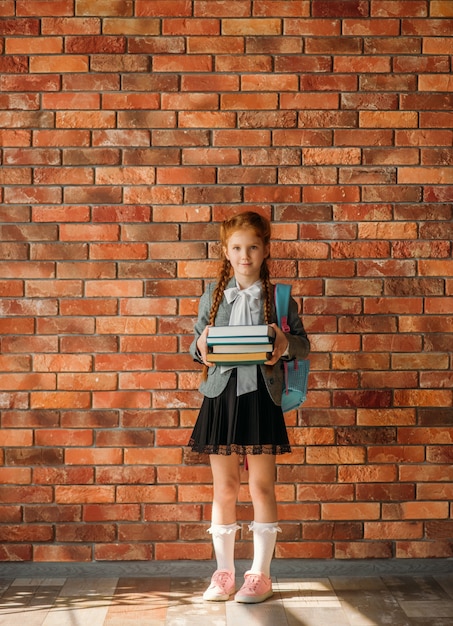 Écolière mignonne avec cartable détient pile de manuels