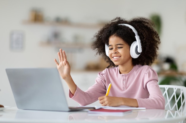 Écolière noire joyeuse ayant l'intérieur de la maison de classe en ligne