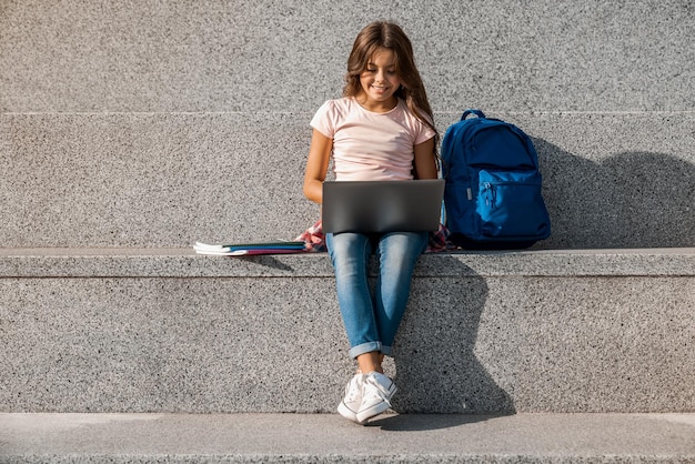 Écolière préadolescente assise sur les escaliers à l'extérieur et utilisant un ordinateur portable