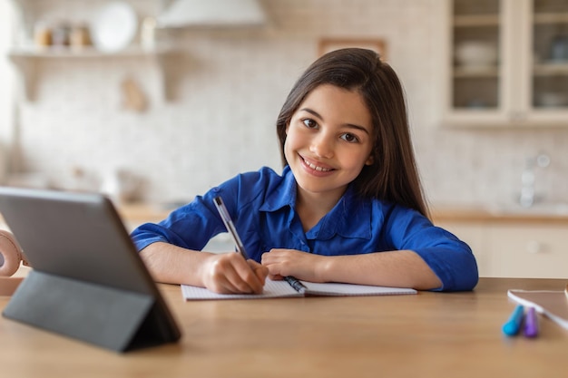 Écolière prenant des notes à l'école grâce à une tablette numérique depuis la maison