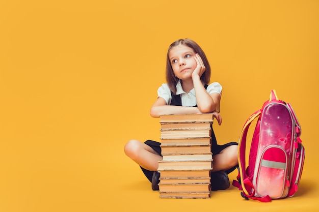 Écolière réfléchie assise derrière une pile de livres avec sac à dos concept d'apprentissage et d'école