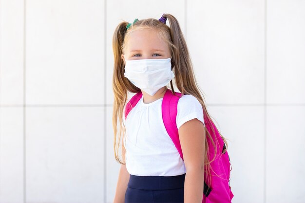 Écolière se tient avec un sac à dos dans un masque médical de protection