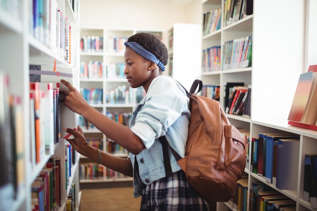 Écolière en sélectionnant le livre de l'étagère à livres dans la bibliothèque