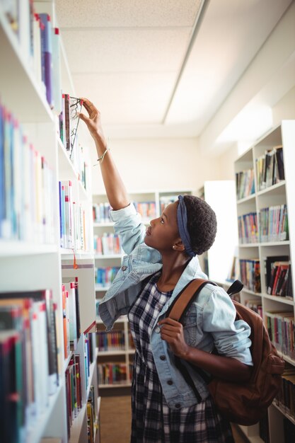 Écolière en sélectionnant le livre de l'étagère à livres dans la bibliothèque