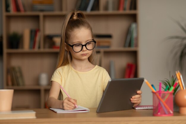 Écolière sérieuse à l'aide de tablette numérique à faire ses devoirs à la maison