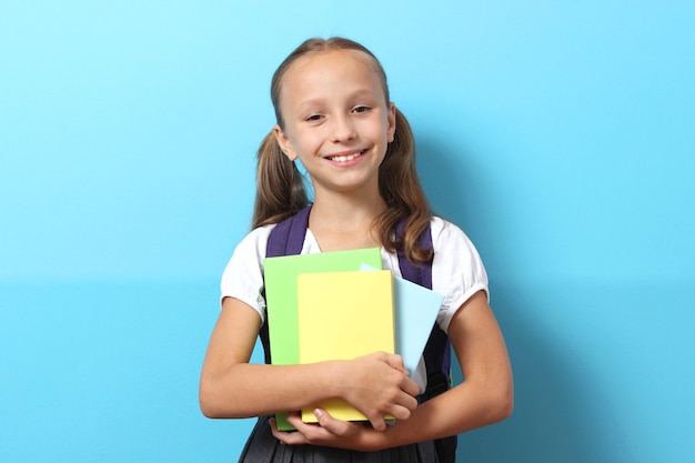 Écolière souriante mignonne avec un sac à dos d'école sur un fond coloré