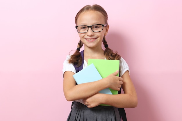 Écolière souriante mignonne avec un sac à dos d'école sur un fond coloré