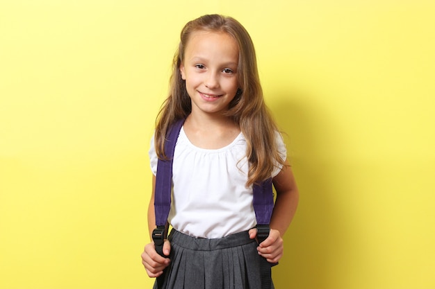 Écolière souriante mignonne avec un sac à dos d'école sur un fond coloré