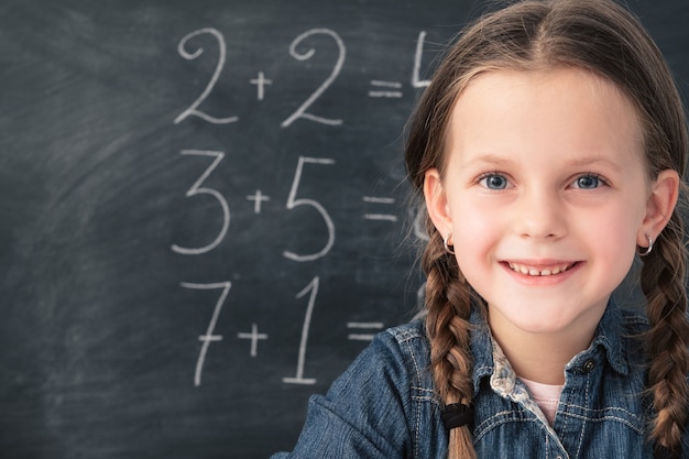 Écolière souriante avec des nattes. Sommes mathématiques sur tableau noir derrière elle