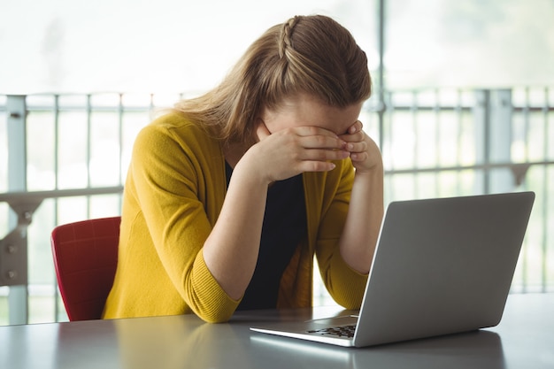 Écolière triste avec ordinateur portable sur la table dans la bibliothèque