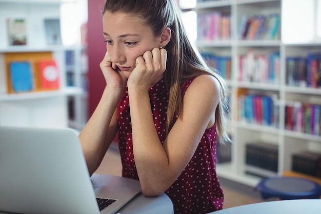 Écolière triste regardant un ordinateur portable dans la bibliothèque