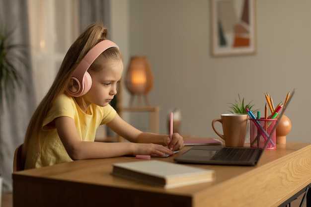 Écolière utilisant un ordinateur portable et prenant des notes à faire ses devoirs à la maison