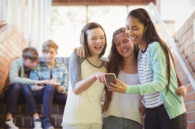 Écolières souriantes à l'aide de téléphone portable dans le couloir