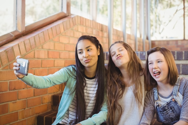 Écolières souriantes assis sur l'escalier prenant selfie avec téléphone mobile