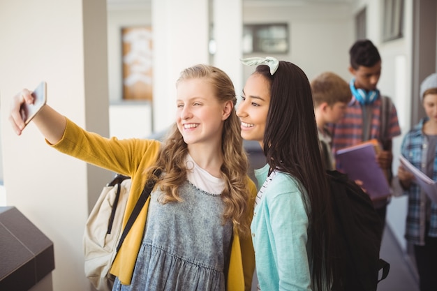 Écolières souriantes prenant selfie avec téléphone portable dans le couloir