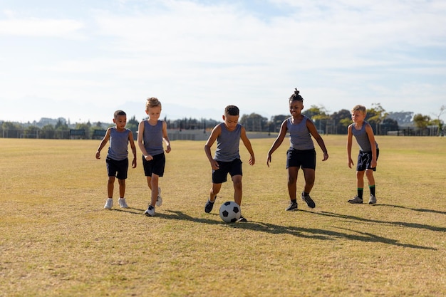 Écoliers élémentaires multiraciaux jouant au football sur le terrain de football de l'école contre le ciel