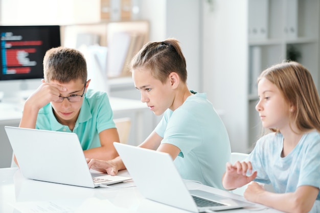 Écoliers mignons assis par un bureau en classe tout en travaillant sur des projets individuels après les cours