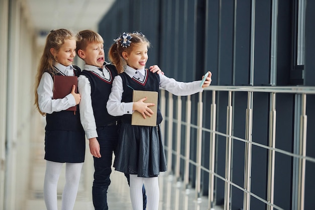 Écoliers en uniforme avec téléphone et faisant selfie dans le couloir Conception de l'éducation