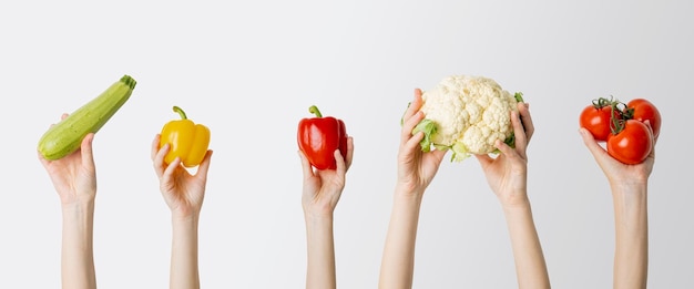 Collage avec des mains féminines tenant du courgette, du poivre, du chou-fleur, de la tomate sur fond blanc.