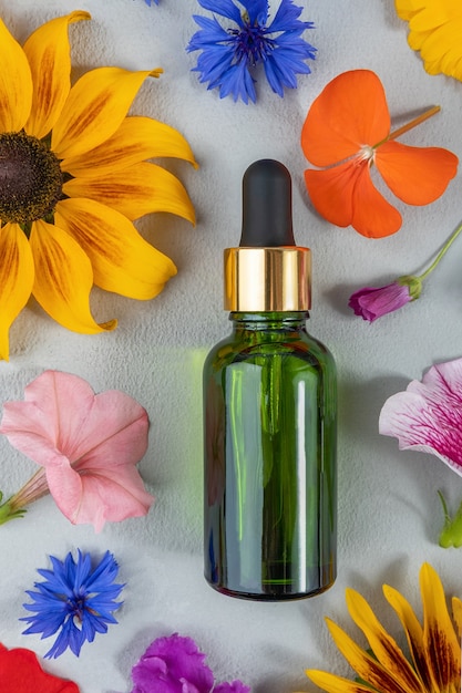 Collagène anti-âge, sérum facial ou autre produit cosmétique dans une bouteille en verre vert parmi les fleurs colorées sur fond gris. Maquette de concept cosmétique de Spa biologique naturel Vue de dessus.